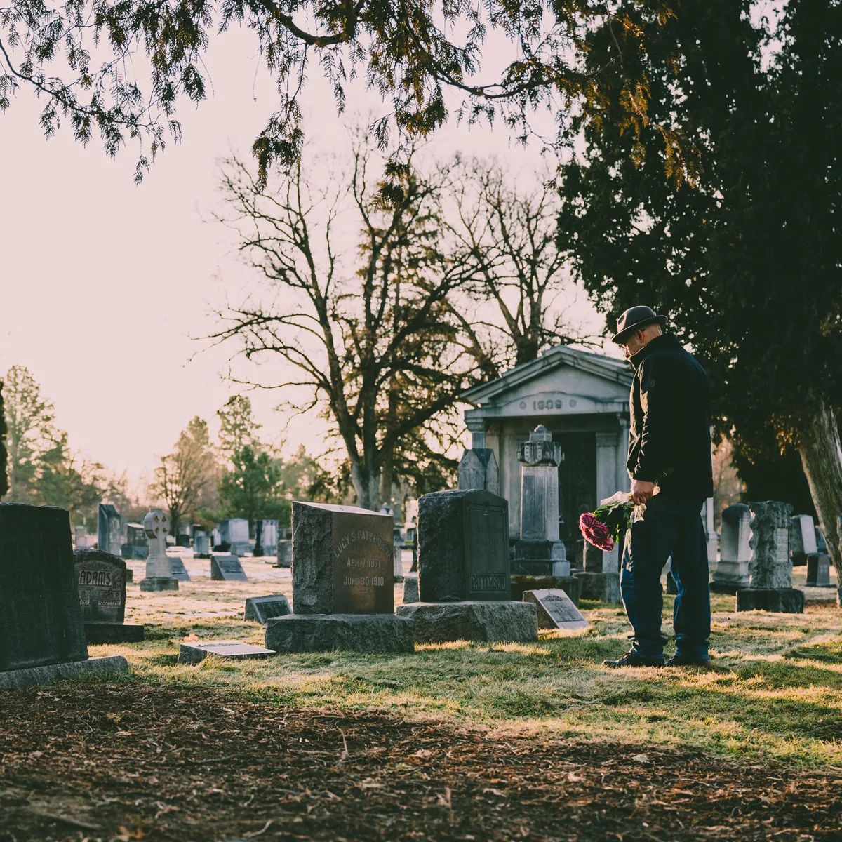 Mann steht mit Blumen an einem Grab auf einem alten Friedhof