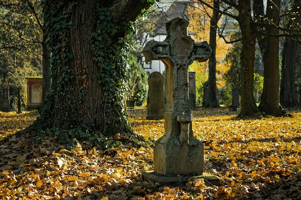 Steinkreuz auf einem Friedhof im Herbstlaub
